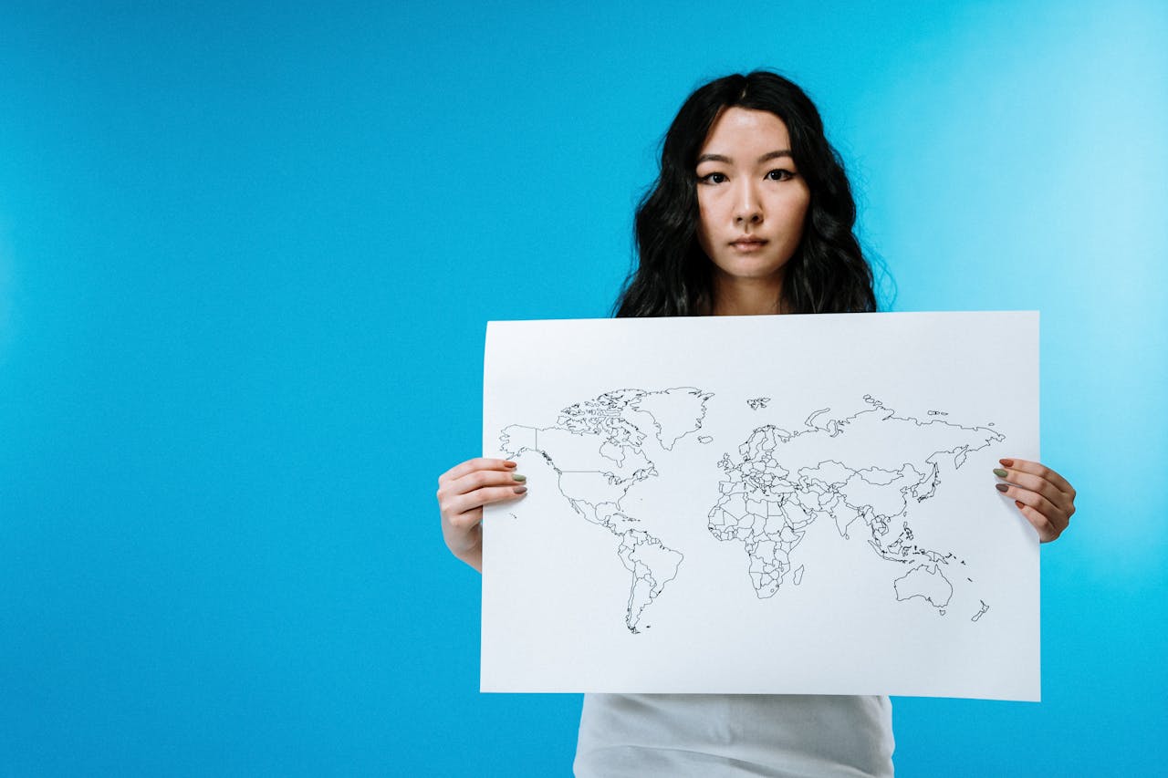 Portrait of a young woman holding a world map against a vivid blue background.